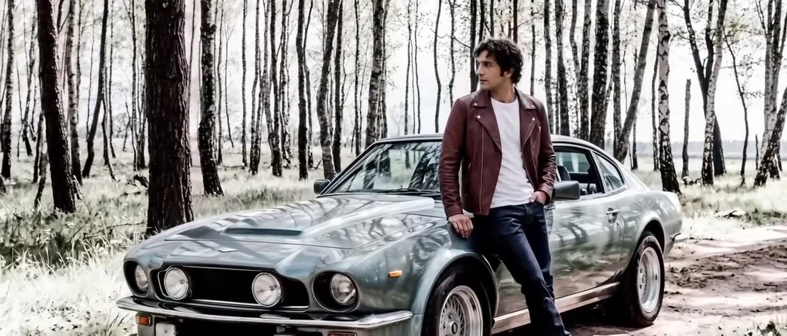 Man in a Heinz Bauer leather jacket beside a classic sports car in a birch forest